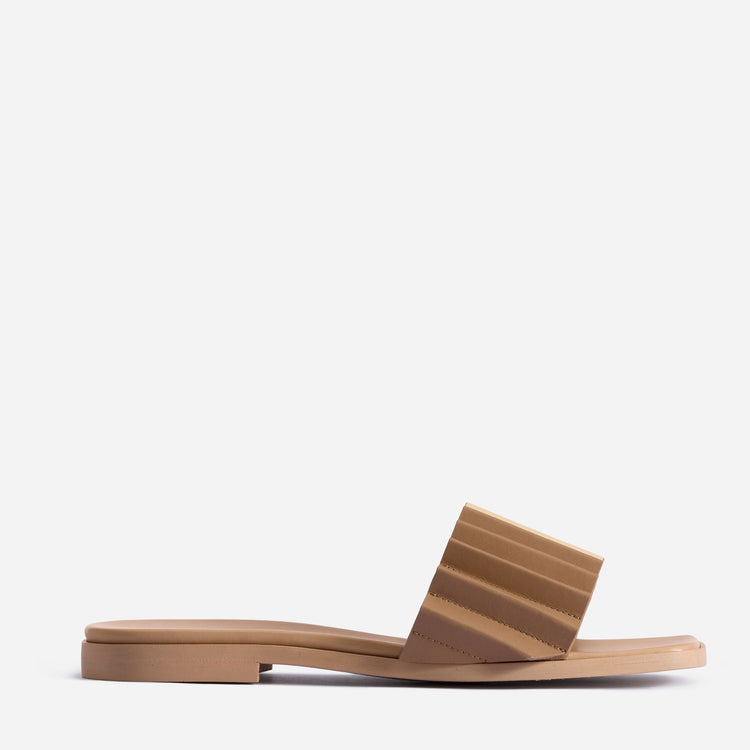 Side view of tan-brown sandal. Back of sandal is slightly raised via 1-inch heel. Wide, single strap across the middle-front features ridged design.