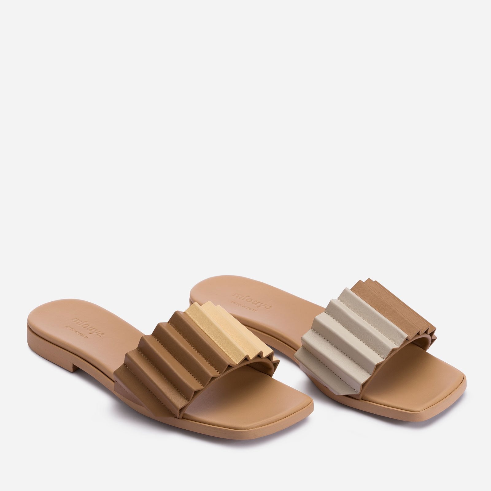 Angle view. Left sandal strap features brown color on left half, white on right half. Right sandal strap features light cream color on left half, brown on right half. The word 'mlouye' is printed on top heel portion of the sandal.